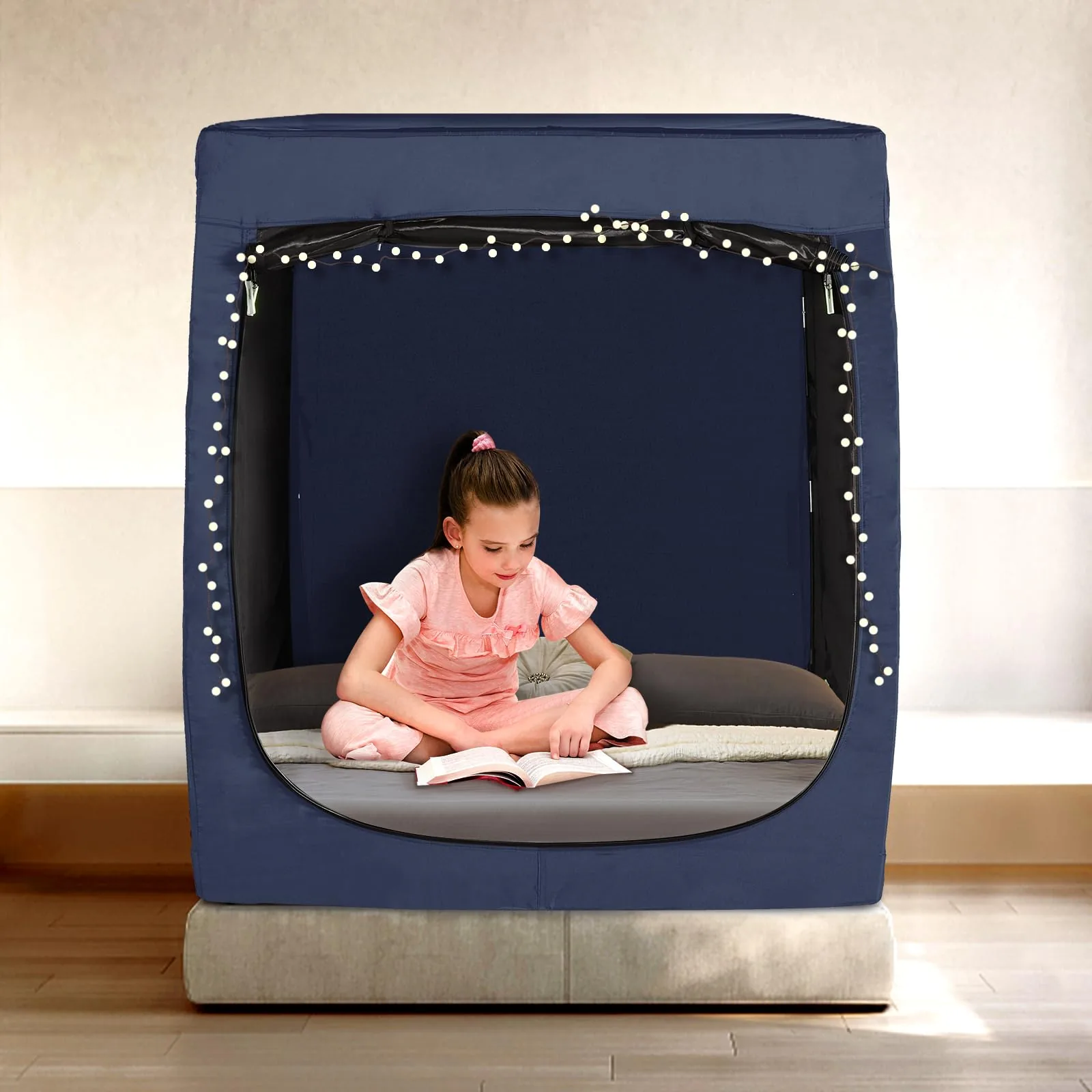 Girl reading inside a navy RIYDH bed tent decorated with string star lights