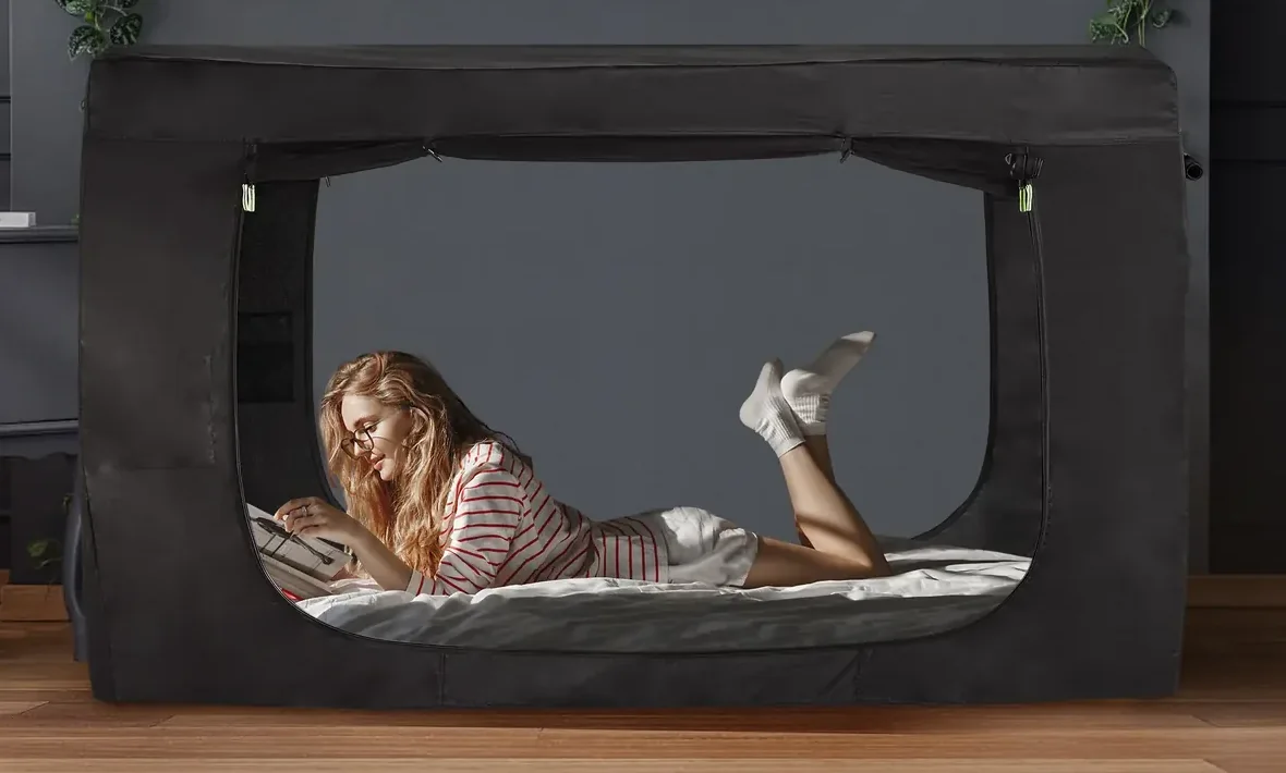 Woman reading inside a black RIYDH bed tent with the front door rolled up